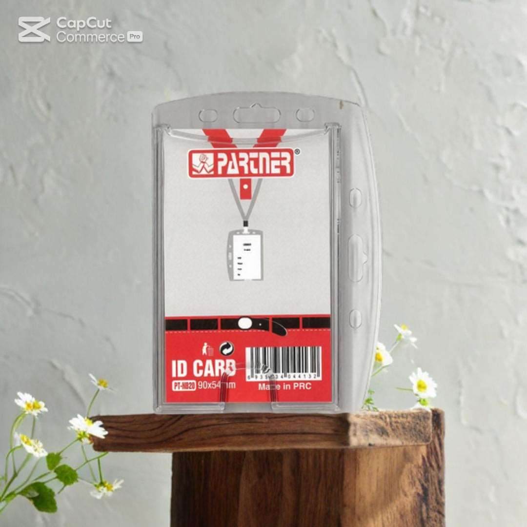 The Partner ID Card Case by Family Book Shop, a transparent vertical badge holder for 90x54mm ID cards, features a red and white label and comes with a lanyard. It's elegantly showcased on a wooden surface decorated with small white flowers.