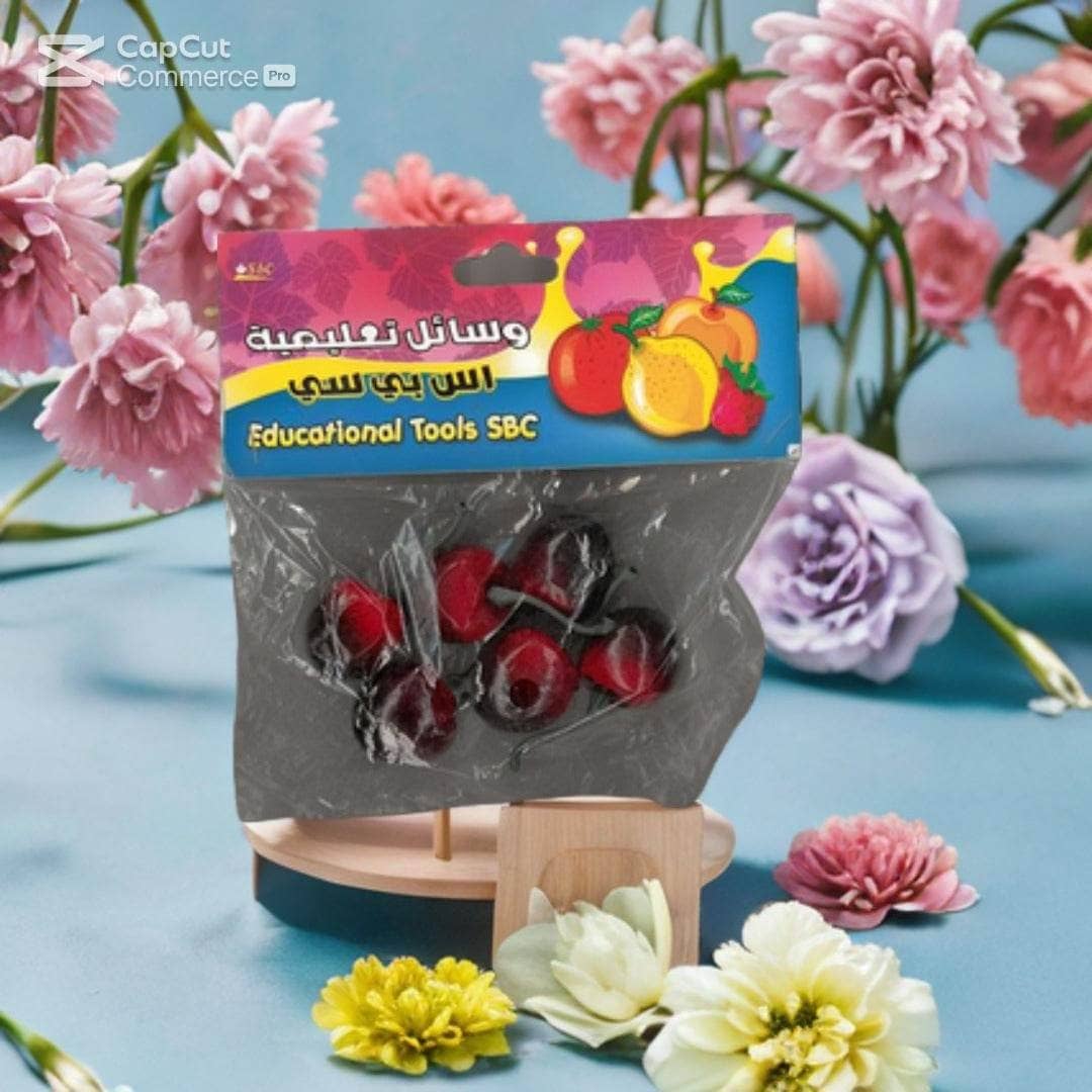 A set of "SBC Educational Fruit Models: Realistic Cherry Learning Tools" from Family Book Shop is shown on a blue surface with pink roses and purple carnations, providing hands-on learning for early education.