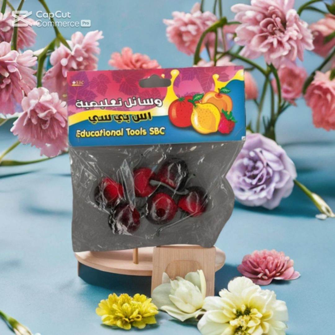 A set of "SBC Educational Fruit Models: Realistic Cherry Learning Tools" from Family Book Shop is shown on a blue surface with pink roses and purple carnations, providing hands-on learning for early education.